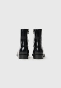 Botas negras de cuero hasta el tobillo con un acabado liso, punta redondeada y cremallera lateral. Cuentan con una suela resistente y un detalle de costura distintivo.