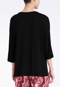 Maglia nera, comoda e larga, con maniche a tre quarti e scollo ampio, abbinata a pantaloni a fantasia rossi e bianchi. Tessuto dalla consistenza liscia.