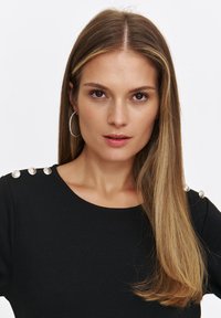 Czarna sukienka z trzema dekoracyjnymi guzikami na ramieniu, okrągłym dekoltem i gładką fakturą materiału. Modelka z długimi włosami i kolczykami w kształcie kół.