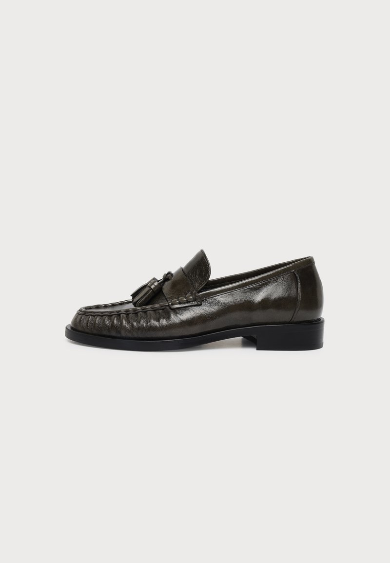 Mocassin à pampilles en cuir marron foncé avec un petit talon et une couture moc toe, montré de profil sur un fond uni.