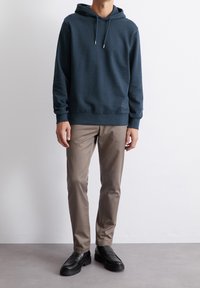 Marintröja med huoodie och justerbara snoddar; ihop med beige slim-fit byxor och svarta loafers på ett grått golv.