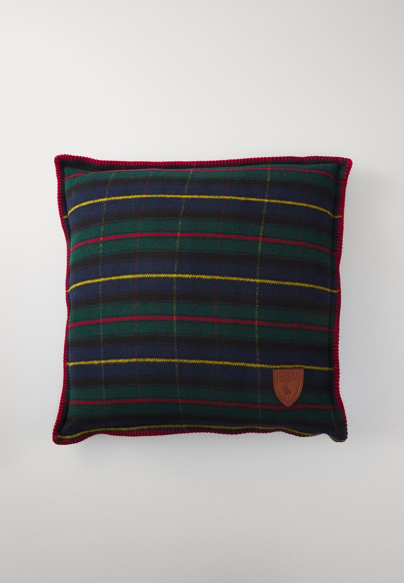 Square pillow with a green and navy plaid pattern, accented by red and yellow stripes. Features a brown leather logo patch and red trim.
