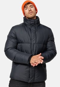 Puffjakke i mørk navy med høj krave, horisontal quiltet design og forlommer. Båret med en orange strikbeanie.