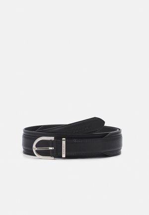Czarny skórzany pasek z srebrną klamrą i logo Calvin Klein, zwinięty i wyeksponowany na jednolitym jasnym tle.