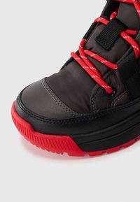 Schwarzer und grauer synthetischer Sneaker mit roten Schnürsenkeln und Gummisohle. Verfügt über ein strukturiertes Obermaterial und eine verstärkte Zehenkappe.