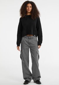 Maglione nero a coste, corto e con maniche ampie, abbinato a pantaloni cargo grigi con tasche laterali e una vestibilità rilassata.