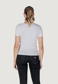 Witte T-shirt met korte mouwen, een ronde hals, een aansluitend ontwerp en een gladde textuur, gecombineerd met zwarte jeans met een driehoekig logo op de achterzak.