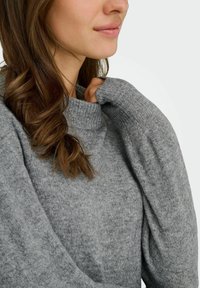 Grau gestrickter Pullover aus Wolle mit einem hohen Kragen und verlängerten Ärmeln, weich in der Textur und mit einem dezenten Muster.