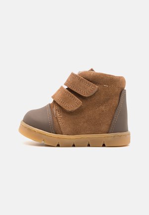 Zapatillas altas de ante marrón con doble tira de velcro, puntera de goma gris y suela de goma texturizada que presenta un discreto patrón de tracción.