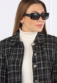 Giacca a scacchi bianco e nero con bottoni metallici, indossata sopra un dolcevita bianco. Modello con occhiali da sole neri rettangolari.