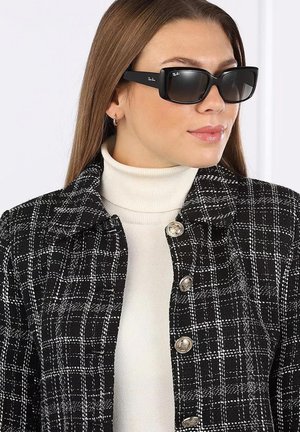 Giacca a scacchi bianco e nero con bottoni metallici, indossata sopra un dolcevita bianco. Modello con occhiali da sole neri rettangolari.