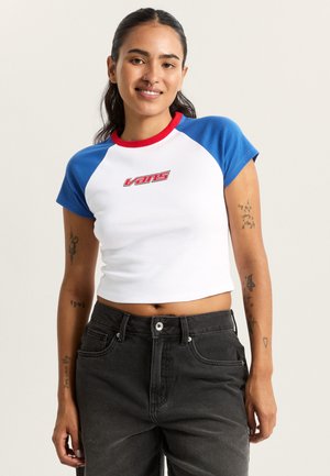 Witte cropped top met blauwe mouwen en rood kraagje. Voorzijde heeft het "Vans"-logo in het rood. Gedragen met donkere high-waisted jeans.