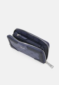 Portefeuille zippé marine en tissu texturé, avec quincaillerie en tonalité argentée, compartiments intérieurs et détails de logo en relief.