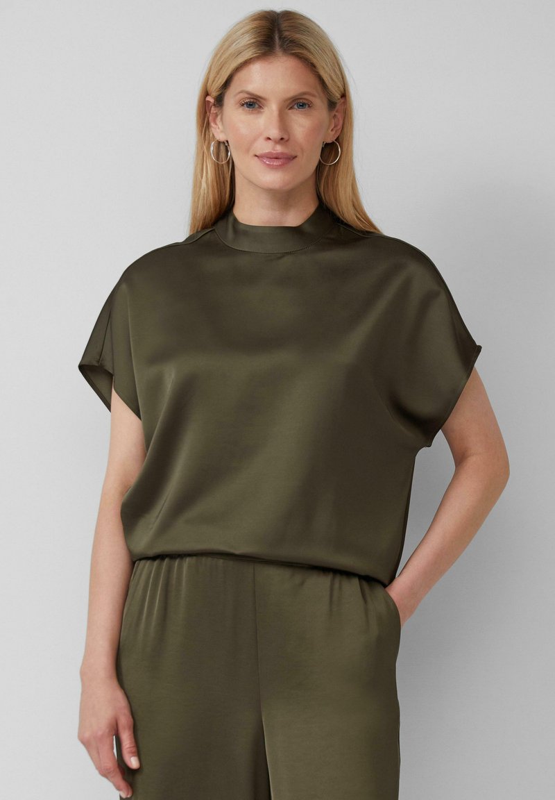 Haut vert olive à manches courtes avec un col montant, en tissu lisse et brillant, présentant une coupe décontractée et un drapé subtil.