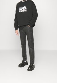 Sudadera negra con el logo blanco de "KARL LAGERFELD", combinada con pantalones gris oscuro y mocasines negros. Diseño simple y casual con un corte relajado.