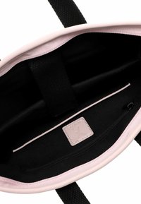 Interno della borsa in pelle vegan rosa con fodera in tessuto nero, tasca con cerniera e etichetta del marchio. Presenta manici piatti scuri e una texture liscia.