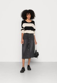 Zwart en beige gestreepte trui met wijde mouwen, gecombineerd met een grijze denim knoopdown midi-rok. Zwarte loafers en een kleine handtas.