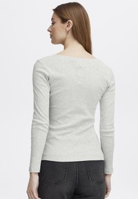 Lys grå langermet topp med scoop-back, ribbet tekstur, tettsittende design, kombinert med mørke jeans. Ingen synlige logoer eller mønstre.