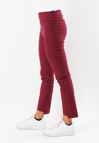 Pantaloni stretchy borgogna con vita alta, vestibilità aderente e orli spaccati. Abbinati a sneaker bianche per un contrasto.