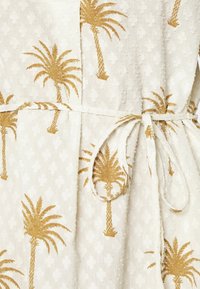 Vestido blanco con bordado de palmeras doradas en una tela texturizada. Incluye un lazo en la cintura para ajuste y un sutil detalle con patrón.