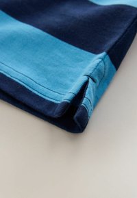 Pamut póló szegély kettős behajtott élekkel, váltakozó világoskék és sötétkék csíkozással, látható varrással és sima textúrával.