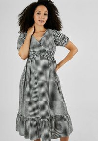 Rochie în carouri alb-negru, cu design înfășurat, mâneci bufante și un tiv stratificat cu volane. Confecționată dintr-un material ușor, potrivit pentru purtat în timpul sarcinii.