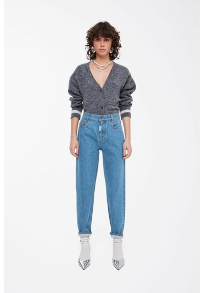 Cardigan grigio in lana con scollo a V profondo, abbinato a jeans in denim azzurro chiaro a vita alta e scarpe argento con punta affusolata.