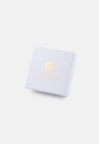 Bijela kutija za poklon s teksturom s zlatnim utisnutim logotipom koji glasi "GINETTE NY." Kvadratnog oblika, čistog dizajna i minimalističkog estetskog stila.