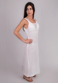 Abito lungo bianco in maglia con spalline sottili, caratterizzato da un design testurizzato e spacchi laterali. Il modello indossa semplici sandali piatti.