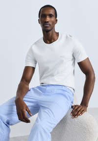 Svetlo siva bombažna majica z okroglim izrezom in subtilno izvezenim logotipom "BOSS", kombinirana z modrimi hlačami s karo vzorcem.