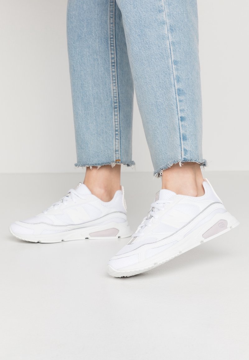 Jambes portant un jean court bleu clair avec des ourlets effilochés et des baskets blanches de sport avec des détails en mesh et synthétiques.