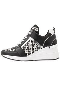 Baskets noires et blanches avec une texture tissée, des accents en cuir lisse, un design à talon compensé et des lacets blancs sur une semelle noire.