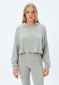 Lyhyt harmaa huppari, jossa on teksturoidusta, pinnalta röpelöisestä kankaasta valmistettu materiaali sekä säädettävä huppu, yhdistettynä matching harmaisiin legginsseihin. Yksinkertainen ja siisti muotoilu.