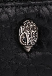 Czarna skórzana powierzchnia o teksturowanym wzorze. Zawiera srebrny metalowy akcent w kształcie dłoni, ozdobiony małymi czarnymi kamieniami szlachetnymi.