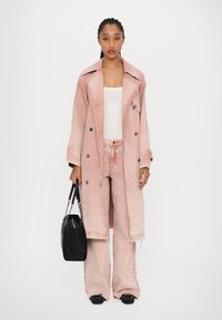 Ružičasti denim trench kaput s detaljima na dugmadima, uparen s odgovarajućim širokim hlačama. Bijela majica i crna torba za ruke upotpunjuju kombinaciju. Crne cipelice s metalnim šiljcima su vidljive.