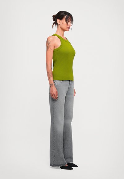 Grön ribbad linne i kombination med högmidjade, vida, blekgrå jeans. Modell vänd åt sidan, med svarta ballerinaskor och synliga tatueringar.