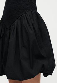 Μαύρη φούστα με μαζεμένο, πλούσιο ύφασμα στη μέση που δημιουργεί σιλουέτα με φουσκωτό τελείωμα.