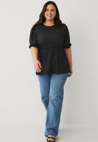 Zwarte textuur top met pofmouwen en een peplum taille, gecombineerd met blauwe flared jeans en zwarte sandalen met open teen. Eenvoudig, casual ontwerp.