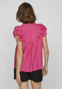 Rosa blus med flätade korta ärmar, samlad bak och en avslappnad passform. Kombinerad med svarta strukturerade shorts. Enkel och avslappnad design.