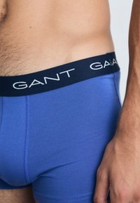 Plave pamučne bokserice s udobnim krojem, s tamnoplavim pojasom s bijelim "GANT" logom. Glatkasti materijal s minimalnim detaljima šivanja.