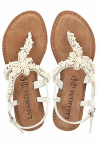 Sandales blanches en thong avec un design floral en coquillages sur une semelle en daim marron, dotées de brides autour de la cheville et d'accents en argent.
