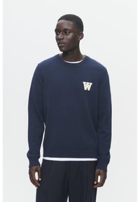 Tumesinine kootud sviiter ribatud varrukate ja äärtega, mille vasakul rinnal on valge "W" logo ning mis on kantud valge sardiini üle.