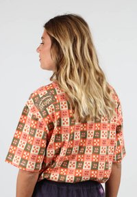 T-shirt à manches courtes en tissu à motif floral coloré. Caractérisé par des carrés oranges, verts et crème avec une étiquette de marque.