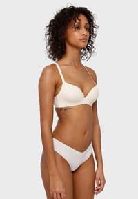 Beige gepolsterde beha met dunne bandjes en een diepe V-halslijn. Bijpassende lage bikini slipjes, gladde textuur, minimalistisch ontwerp.