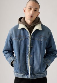 Denim jacket with a light blue wash, shearling collar, and snap-button closure. Features diamond-shaped embroidery and side pockets.