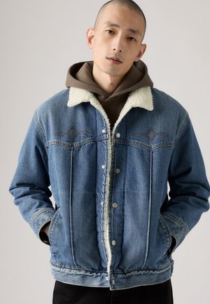 Denim jacket with a light blue wash, shearling collar, and snap-button closure. Features diamond-shaped embroidery and side pockets.