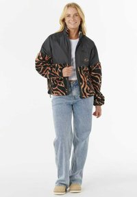 Chaqueta negra acolchada con mangas de forro polar de leopardo; cuenta con una cremallera al frente, cuello alto y bolsillos laterales, combinada con unos jeans azul claro.