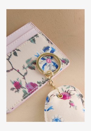 Kartes turētājs ar ziedu rakstu un rozā malu, kam piestiprināts zelta krāsas atslēgu riņķis un ķēde, kā arī atbilstoša ziedu auduma atslēgu piekariņš.