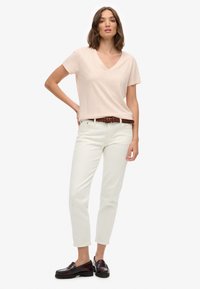Lyserød v-hals t-shirt, hvide lige ben jeans, brun flettet bælte og mørke loafers. Glat stof med en afslappet pasform og korte ærmer.