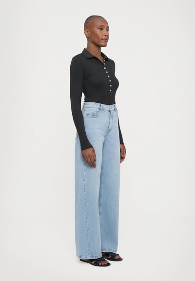 Black long-sleeve polo top with button front, paired with light blue wide-leg jeans and black sandals. Smooth, fitted top, casual, loose bottom.
